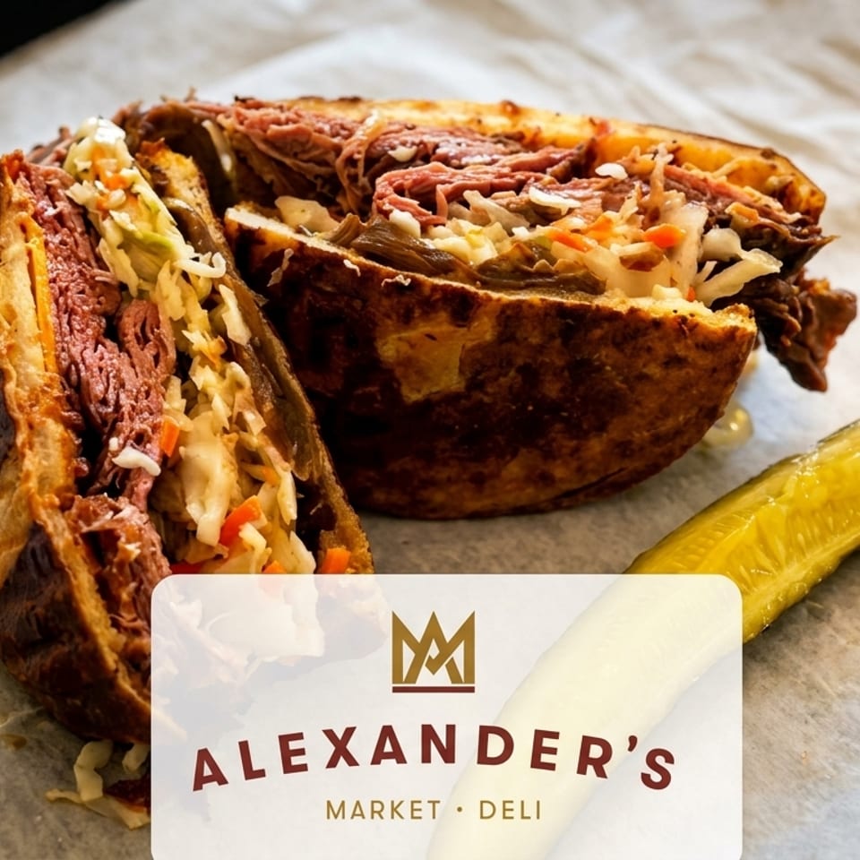 Alexander's Market & Deli Reuben sandwich, cut in half, with a pickle spear on parchment paper.